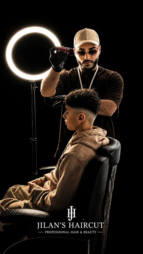 Barbier arbeitet mit dem Trimmer am Übergang eines Fades bei einem jungen Kunden, Studio-Aufnahme mit Ringlicht